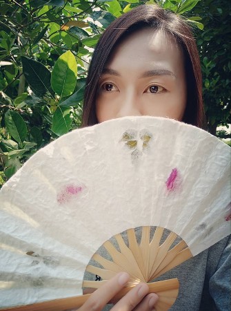 person holding a paper wedding fan with pressed flowers